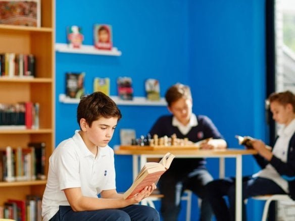Young boy reading a book in a colorful library setting.