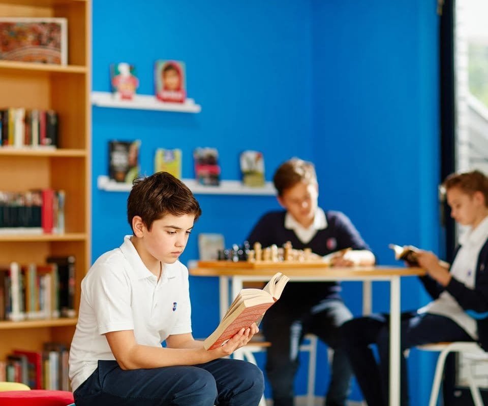 Young boy reading a book in a colorful library setting.