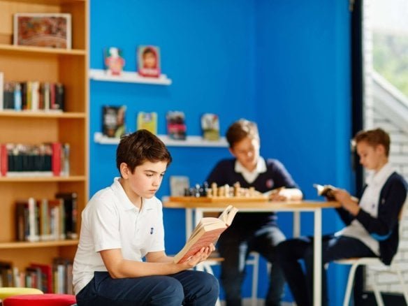 Young boy reading a book in a colorful library setting.