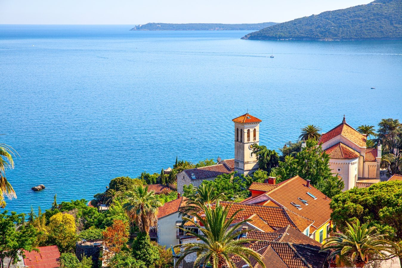 Coastal view of a Mediterranean village with red-tiled roofs, lush greenery, and a calm blue sea, re.