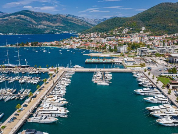 Aerial view of a luxury marina with yachts, surrounded by scenic mountains and a coastal town in Mon.
