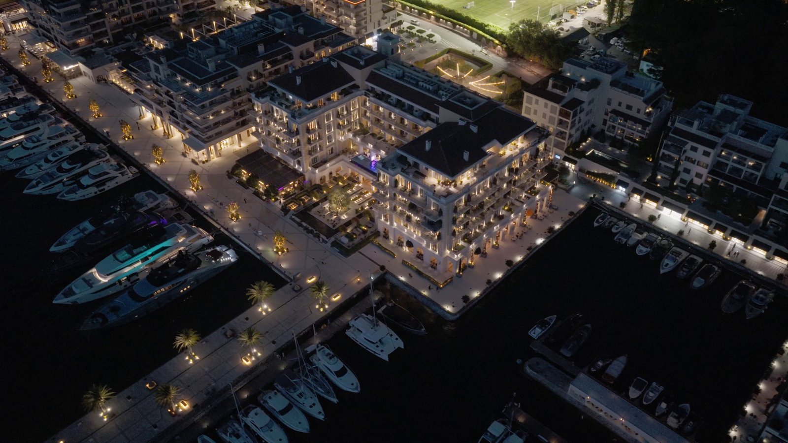 Aerial view of luxury waterfront apartments illuminated at night with marina and yachts.