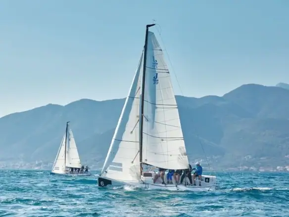 Sailing yacht with crew on the water, mountains in the background, and a clear sky.
