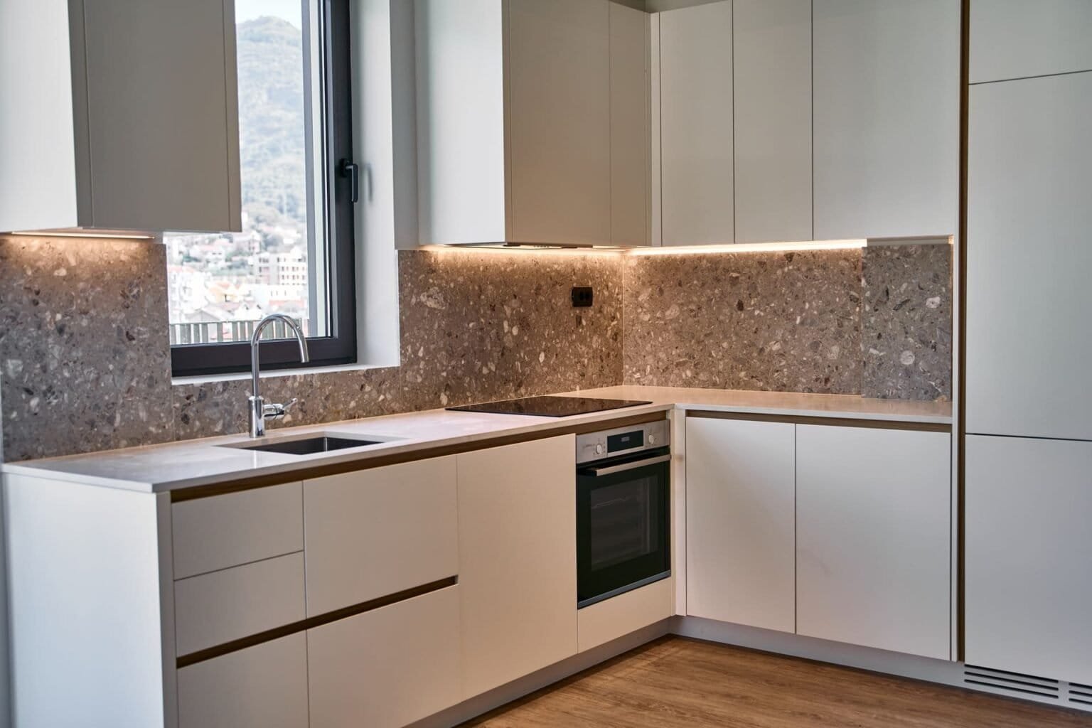 مطبخ عصري بخزائن بيضاء وأسطح عمل من الجرانيت وإطلالة خلابة على الجبال.