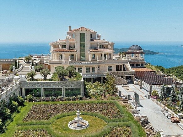 Opulent mansion overlooking the ocean, featuring expansive terraces and lush gardens.