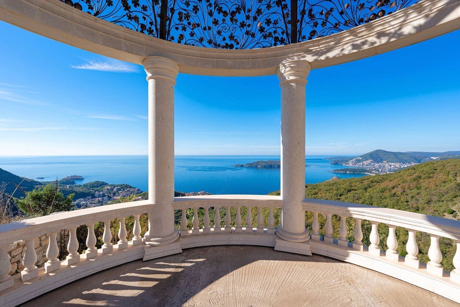 Scenic ocean view from a white balcony with columns and ornate ironwork.
