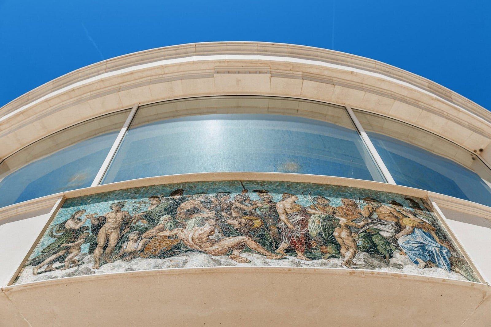 Elegant modern building with large glass windows and a historic mosaic mural.