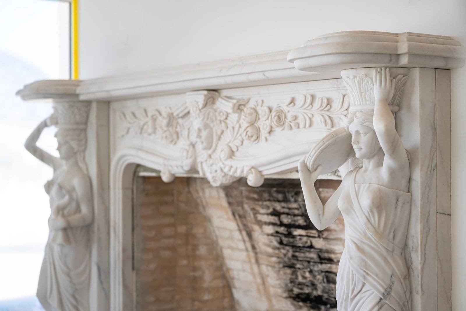 Marble fireplace with classical sculptures and detailed carvings, showcasing luxury and craftsmanshi.