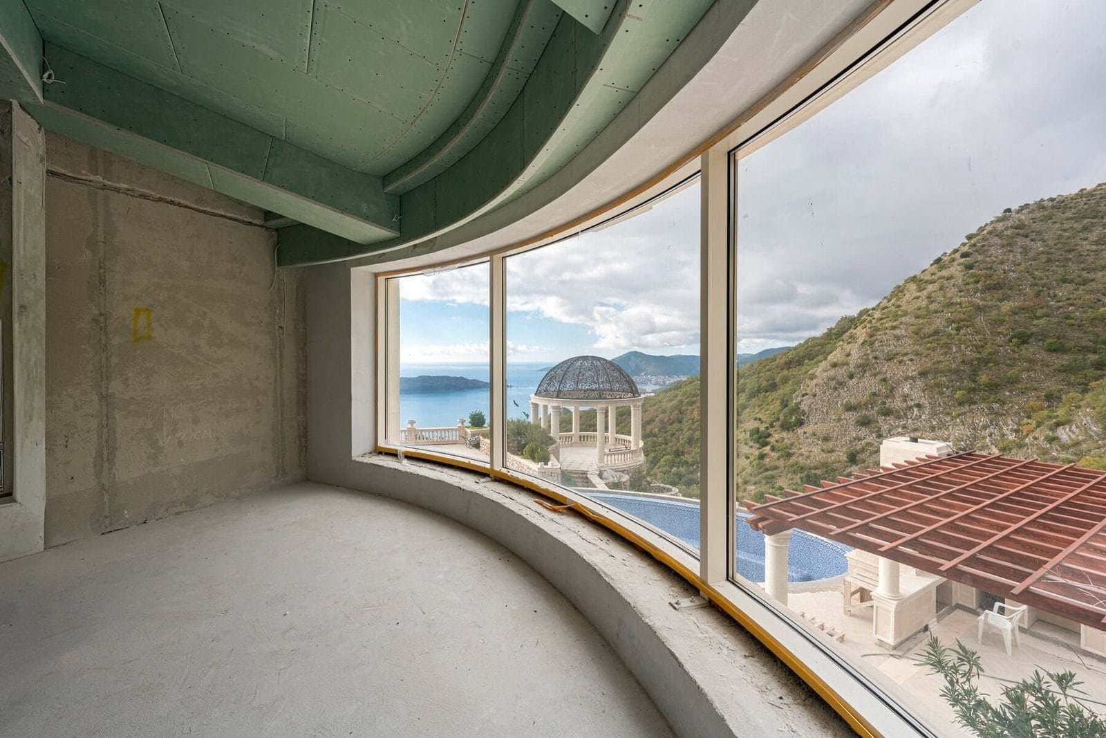 Ocean-view balcony with curved glass railing overlooking the sea and mountains.