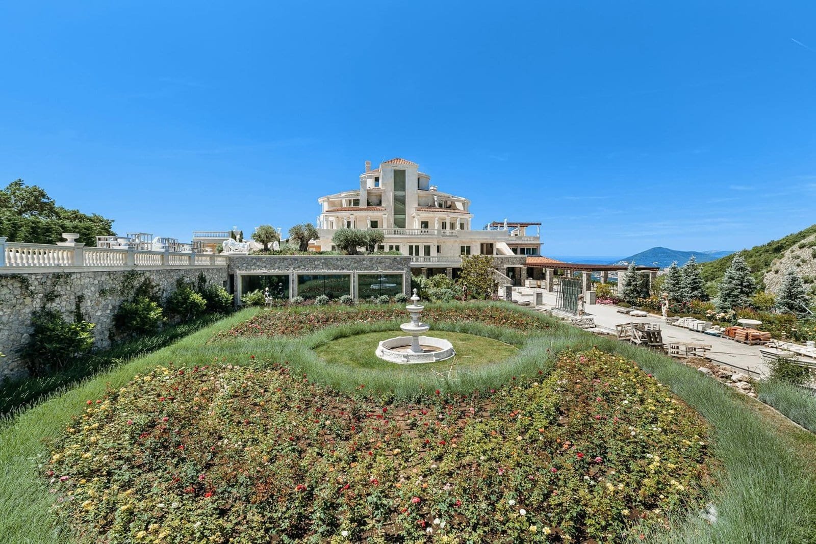 Luxury villa with lush garden and central fountain in a scenic hillside location.