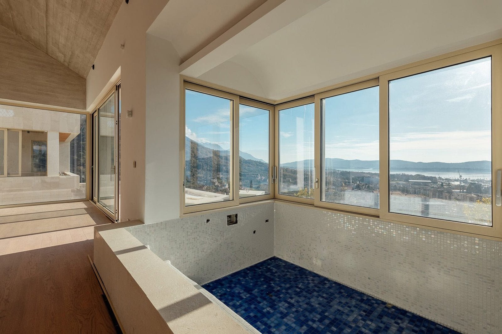 Indoor pool with large windows showcasing scenic mountain and water views.
