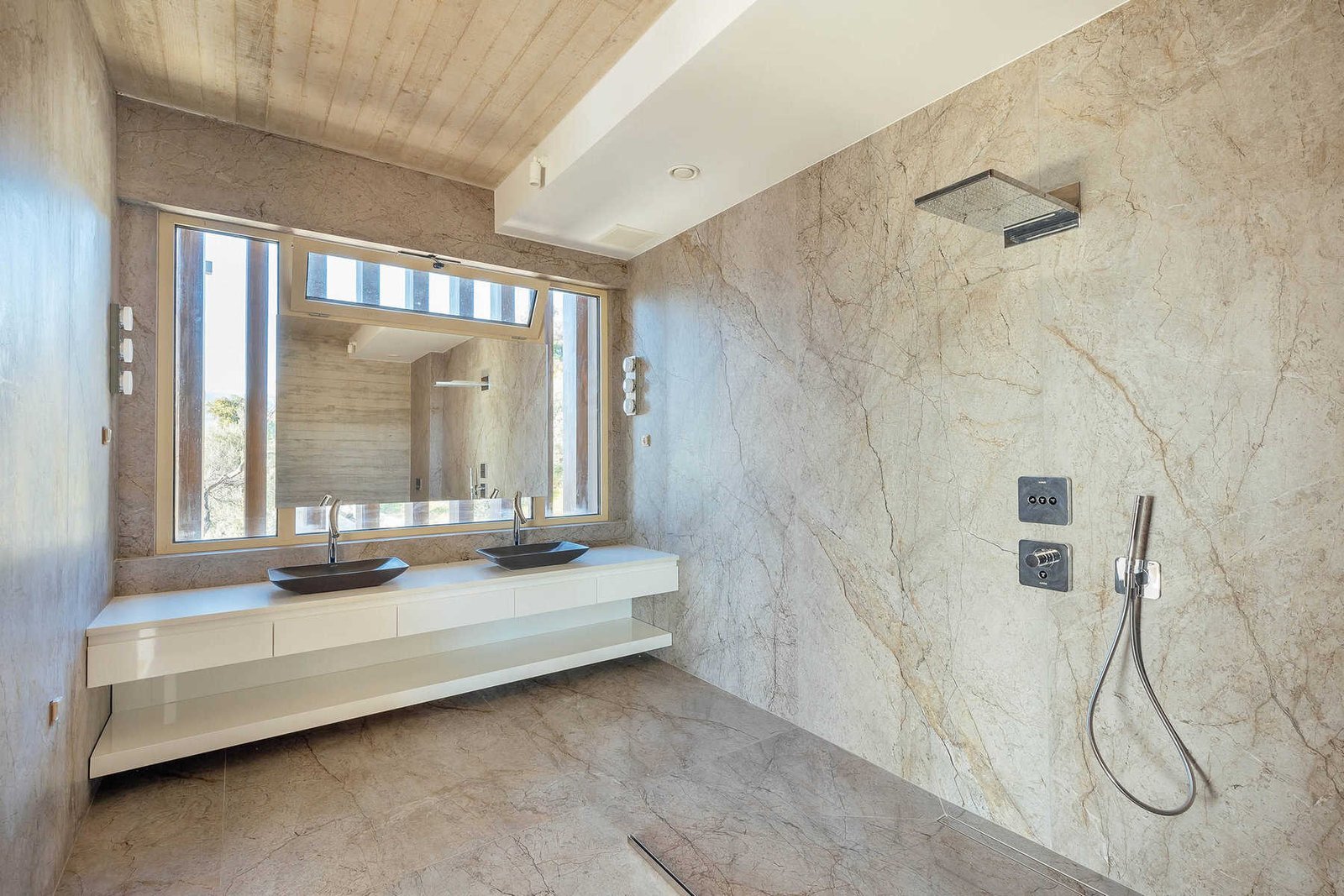 Luxury modern bathroom featuring natural stone walls and flooring, dual sinks, and sleek fixtures fo.