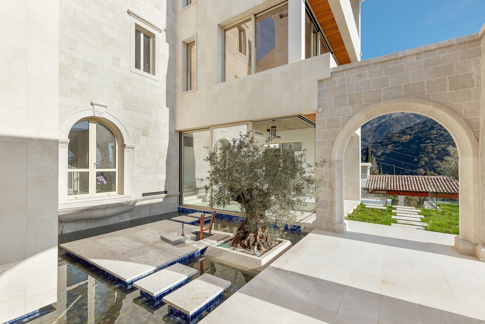 Elegant villa courtyard featuring an olive tree, stone arches, and modern architecture in a scenic m.