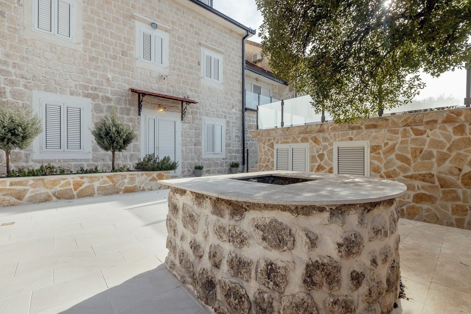 Elegant stone well in a modern estate courtyard with lush trees.