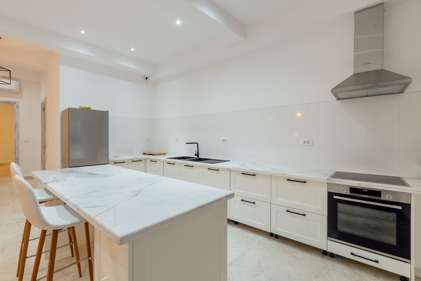 Modern white kitchen with marble countertops and stainless steel appliances.