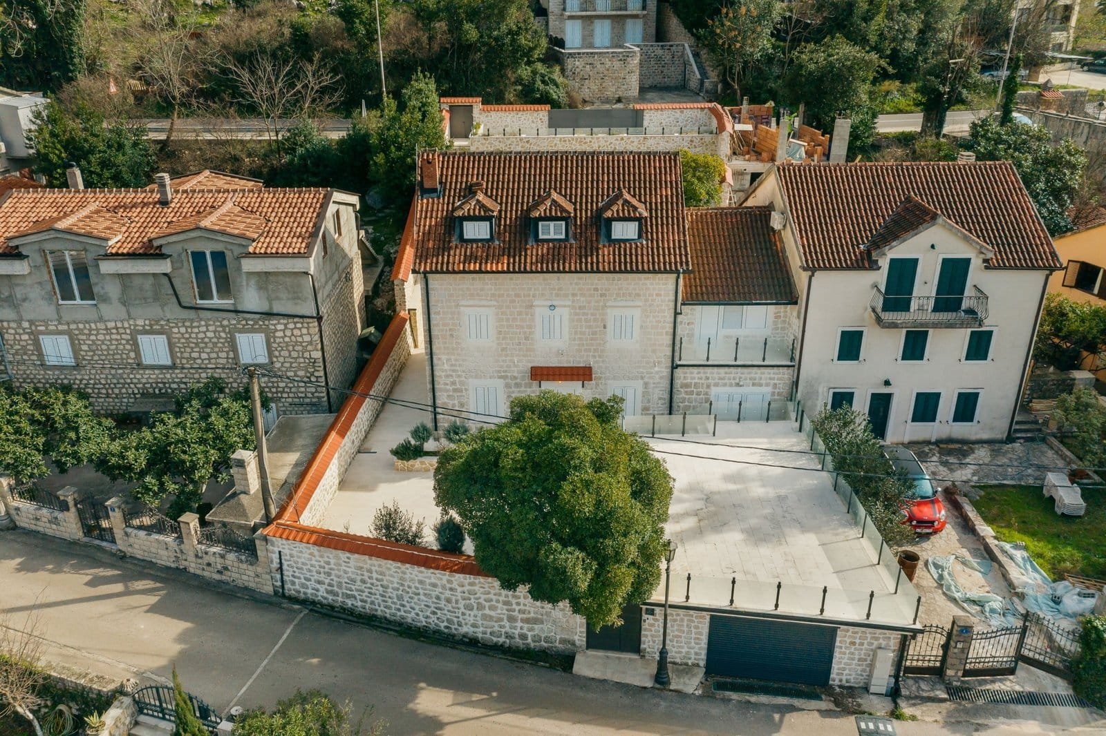 Aerial view of a luxurious villa with a large yard, trees, and gated entrance in a residential neigh.