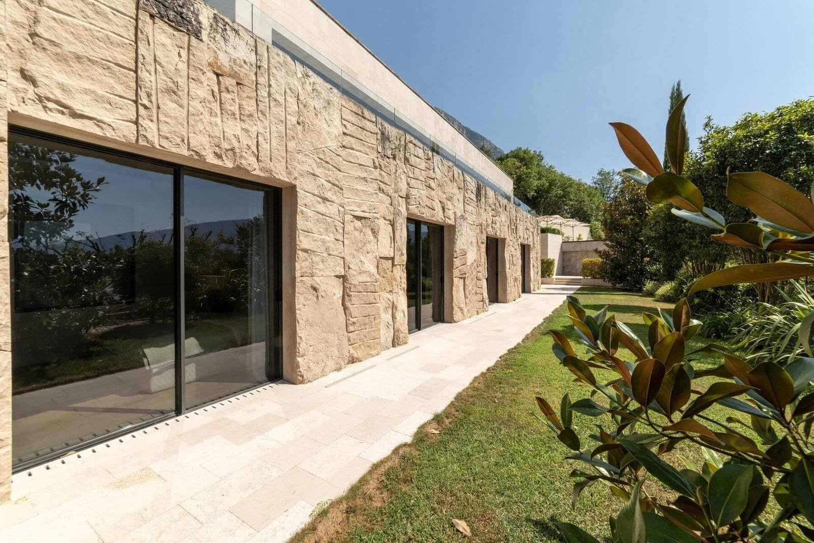 Elegant stone villa with expansive glass doors and landscaped outdoor space.