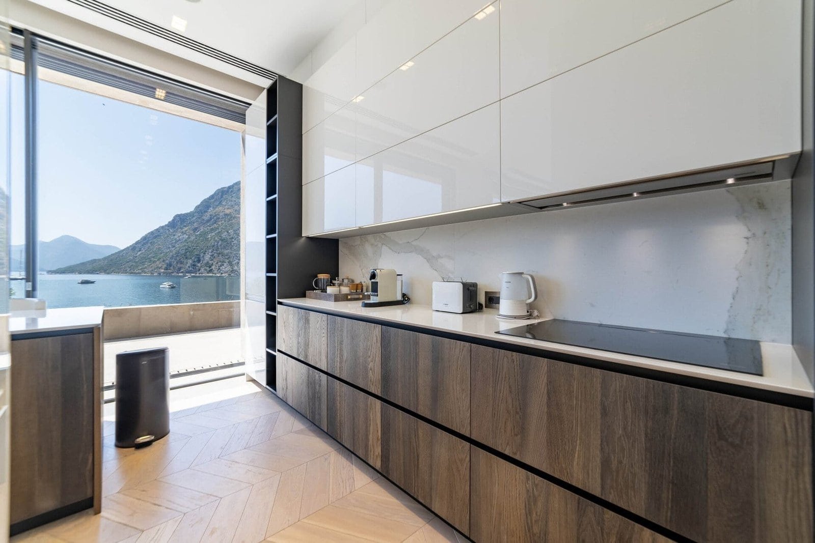Modern kitchen with sleek cabinetry and large window overlooking a lake and mountains.