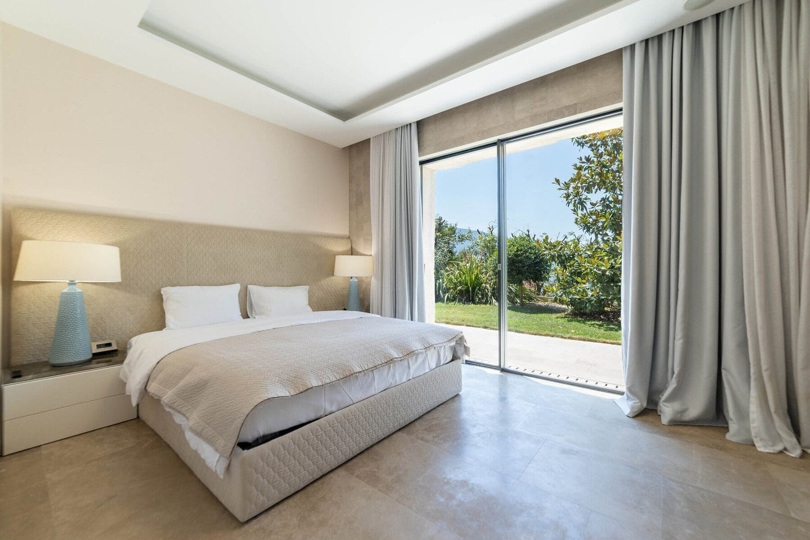 Luxury bedroom with modern decor and large glass doors overlooking lush garden. Perfect for relaxing.