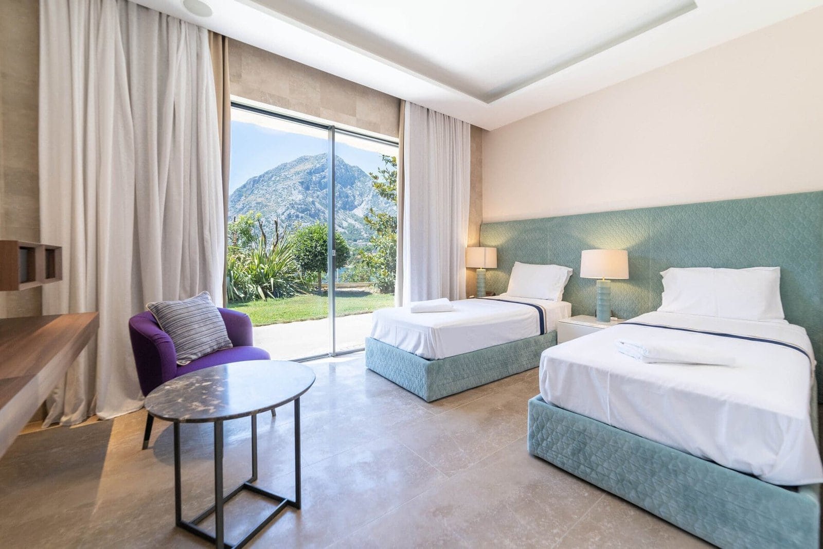 Spacious hotel room featuring two beds, large window with mountain scenery, and contemporary furnish.