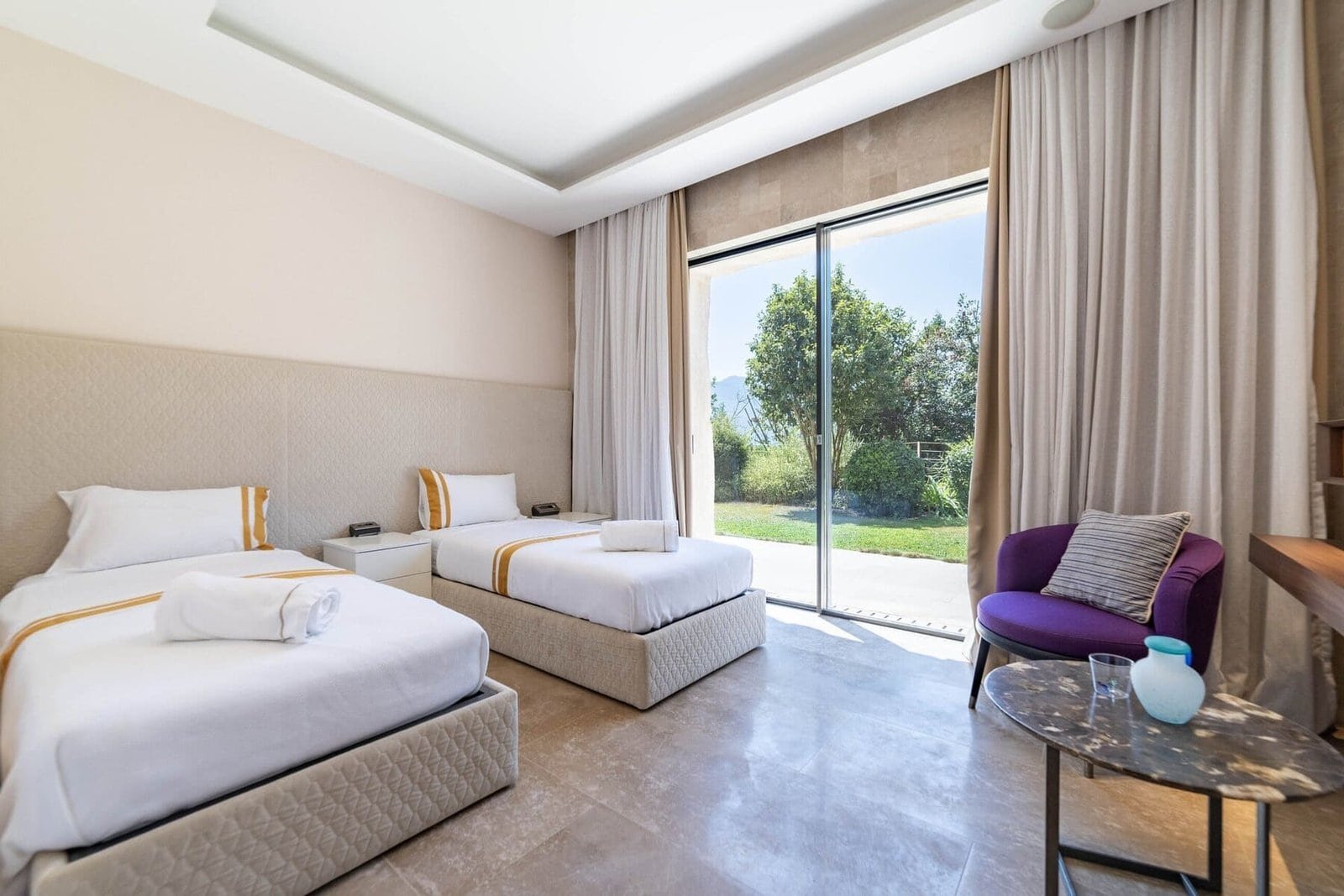 Luxury hotel room with two beds and large glass doors overlooking a lush garden. Modern decor and co.