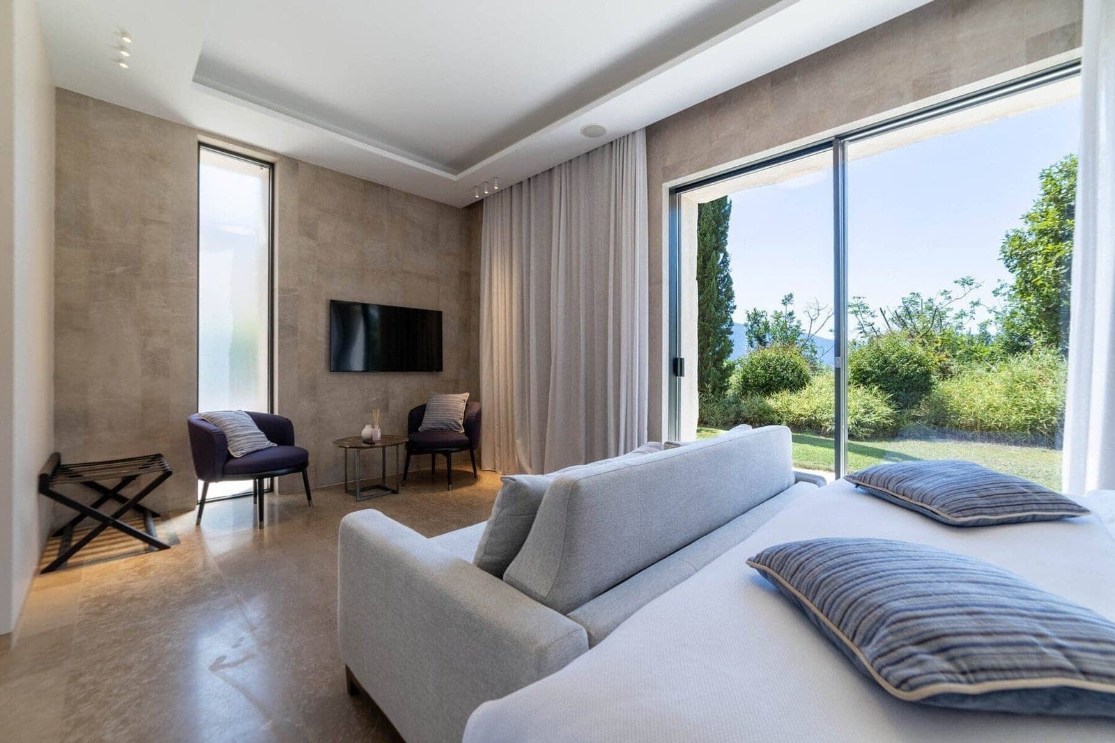 Luxury bedroom with large windows overlooking lush greenery and outdoor landscape.
