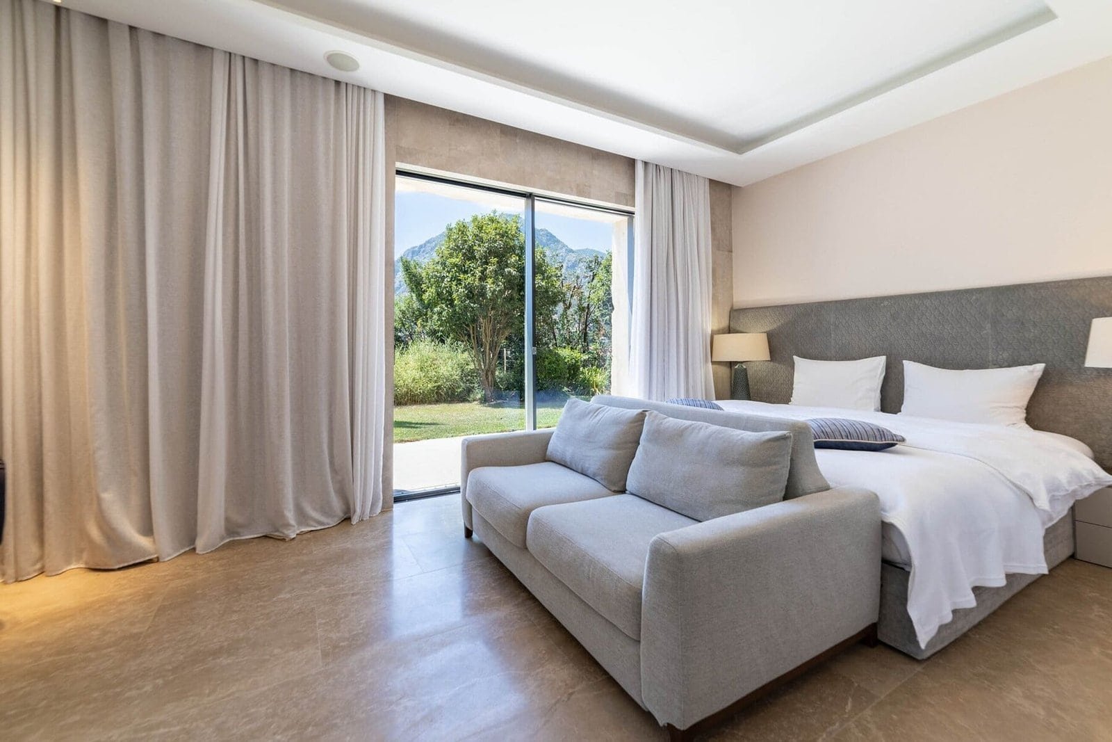 Elegant bedroom with large window overlooking lush greenery and mountains.