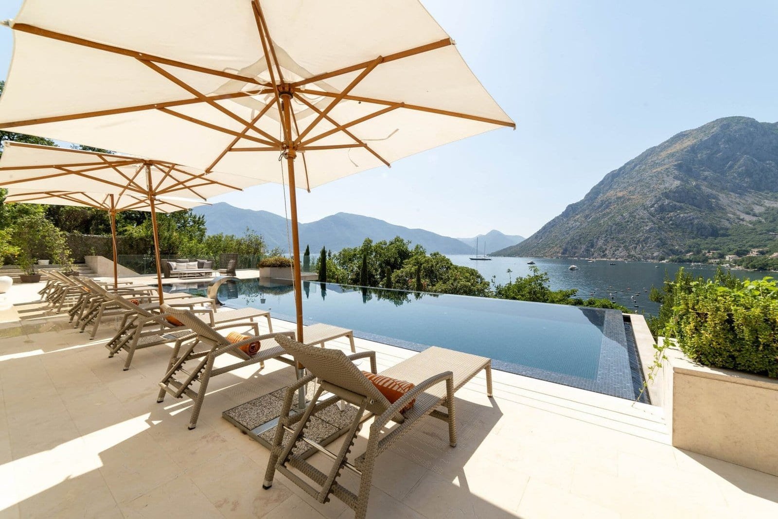 Luxury poolside lounge area with sunbeds and umbrellas overlooking scenic mountains and a serene lak.