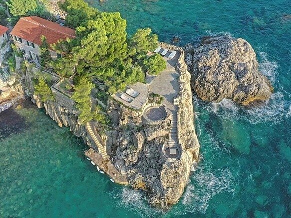 Luxury Montenegro estate on rocky coastline with lush greenery and panoramic sea views.