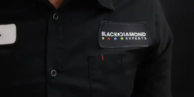 A friendly professional in a Black Diamond Experts shirt stands ready to provide trusted 24/7 plumbing, HVAC, and electrical service.