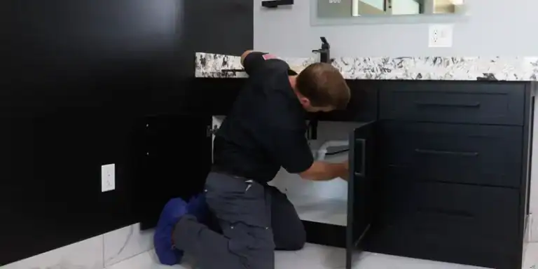 A dedicated technician repairs plumbing beneath a black cabinet, reflecting Black Diamond Experts’ trusted 24/7 home comfort service.