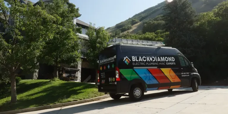 A Black Diamond Experts van, ready for 24/7 AC, plumbing, electrical & drain service, is parked by a home amid Utah hills.