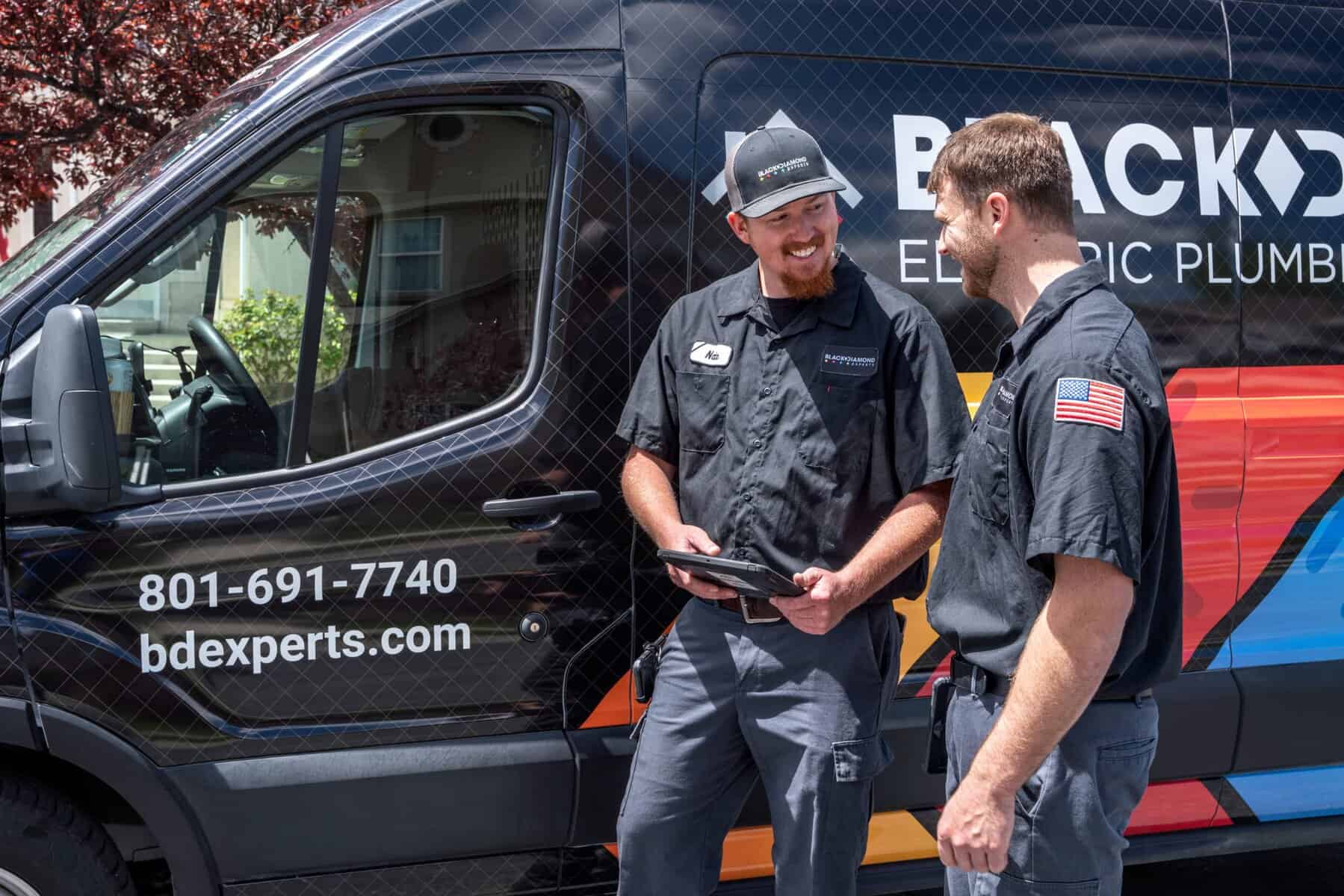 Two Black Diamond Experts in uniform consult by a branded van, ready to deliver trusted 24/7 HVAC, plumbing, and electrical care.