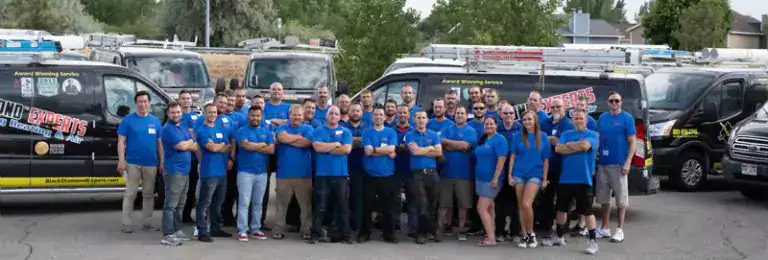 Friendly team members in blue shirts stand by Black Diamond Experts service vans, ready 24/7 for trusted home repairs in Utah.