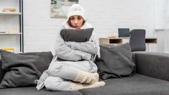 A woman bundled up on her couch looks chilly, reminding Utah families that Black Diamond Experts ensure reliable home comfort 24/7.