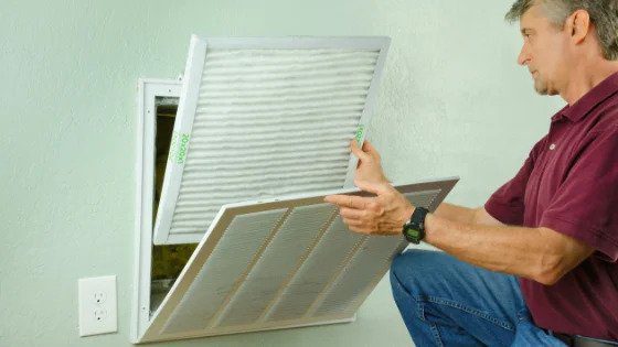 A skilled technician replaces an air filter in a wall vent, ensuring your home’s comfort and safety with trusted local expertise.