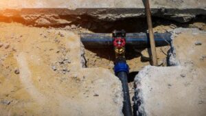 A water pipe with a red valve is expertly installed in a trench, reflecting our trusted 24/7 plumbing and home repair service.