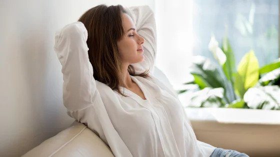 A woman in a white blouse relaxes on her couch, at ease thanks to trusted, 24/7 home comfort and repair services from local experts.
