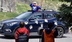 A costumed individual stands through a festively decorated car’s sunroof as two children watch, showing trusted local support and care.