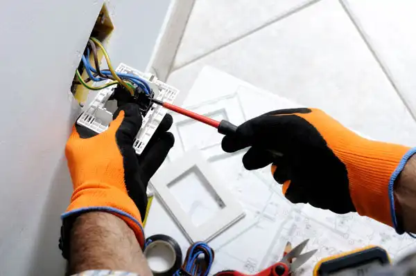 A technician in orange gloves expertly repairs an electrical outlet, showcasing Black Diamond Experts’ trusted, 24/7 home services.