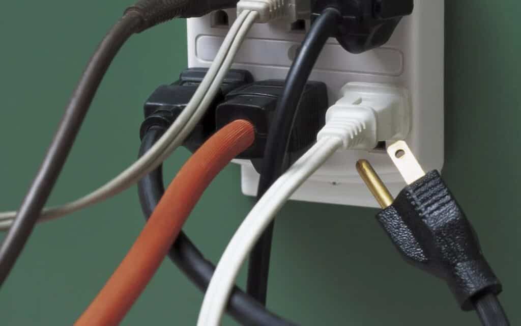 Multiple electrical cords securely connected to a wall-mounted power strip, with one black plug slightly out—for safe, expert service.