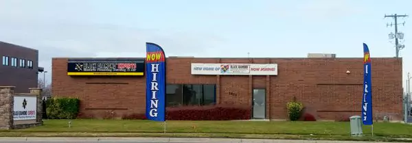A single-story brick building with two "Now Hiring" flags and signage, reflecting a trusted, reliable team always ready to serve.