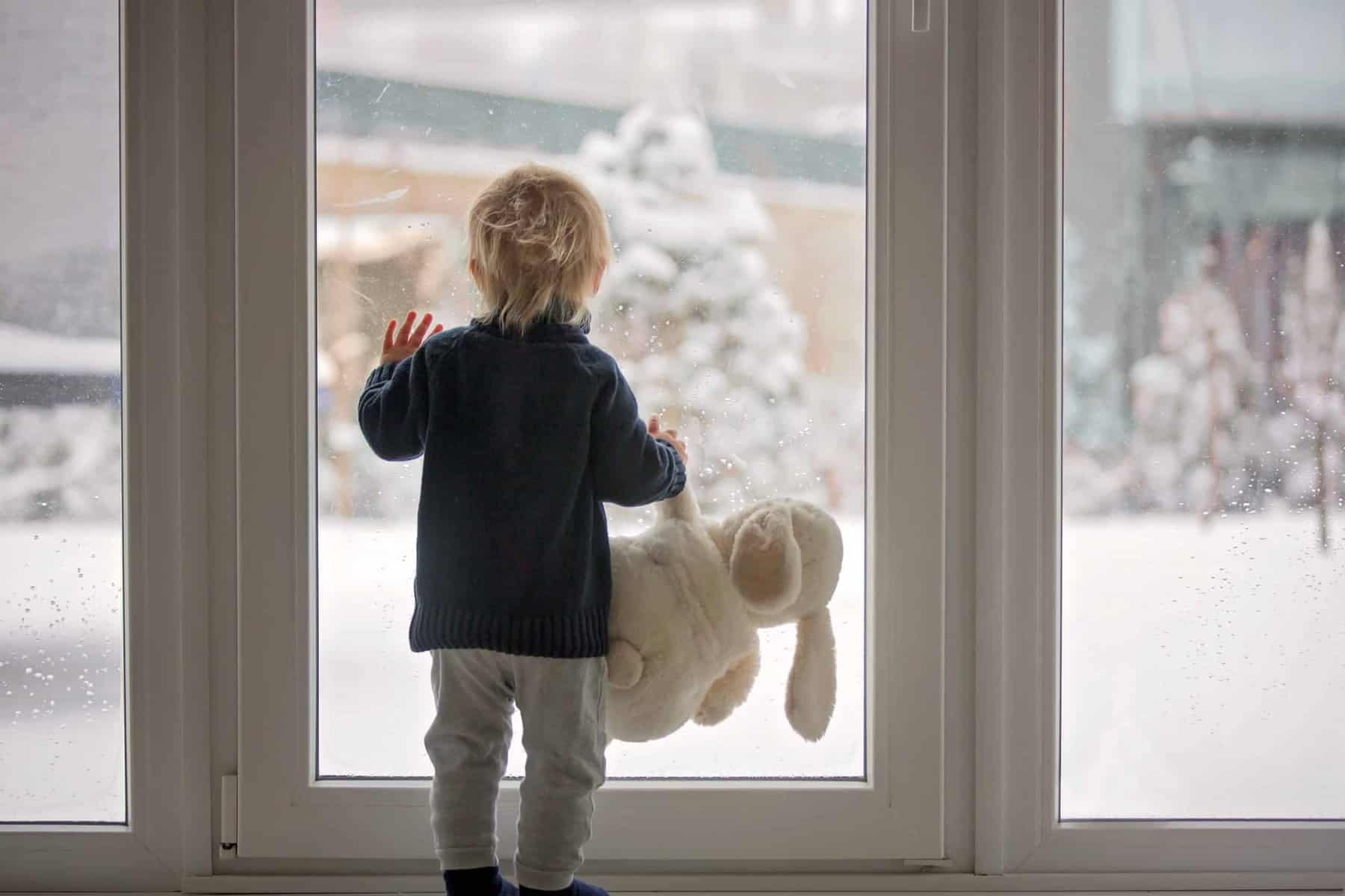 A child with a stuffed animal gazes out a window at snow, feeling safe and cared for by Utah’s reliable home comfort experts.