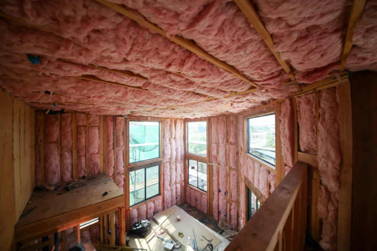 An unfinished room with exposed wooden framing and pink fiberglass insulation along the walls and ceiling, featuring a sturdy workbench beneath sunlit windows. This space reflects the meticulous approach of Black Diamond Experts, Utah’s trusted professionals in electrical, plumbing, HVAC, and drain services. With 24/7 emergency response and a reputation for dependable craftsmanship, our team delivers safe and comfortable solutions—ensuring your circuit breaker installation or any home project is handled efficiently for lasting peace of mind.