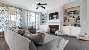 Living room with dark brown hardwood floor and gray L-shape contemporary, book shelf and ceiling fan