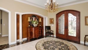 Entry way of a house with white marble, a round black and white is placed on the floor, gold color chandelier hanging on the ceiling.