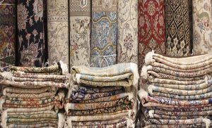 Folded and stacked rugs in front of the rolled Persian rugs placed against the wall.