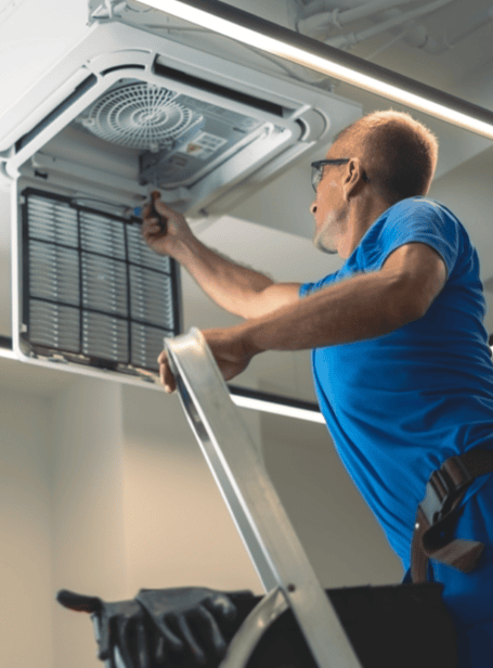 Air conditioning technician servicing ceiling unit at Blue Box Self Storage facility.