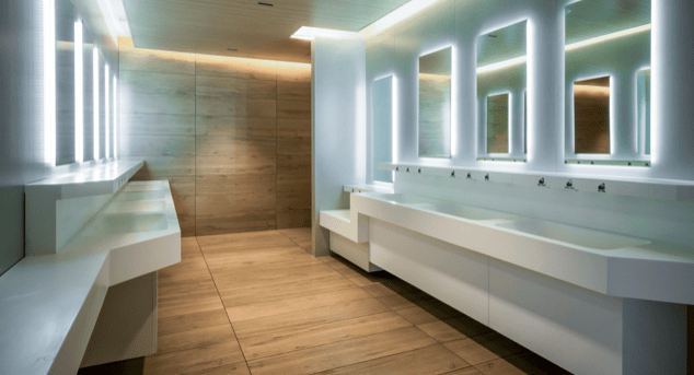 Modern public restroom with illuminated mirrors and wooden flooring.