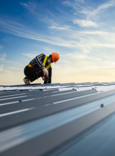 Roof installation worker inspecting metal roofing panels at sunset.